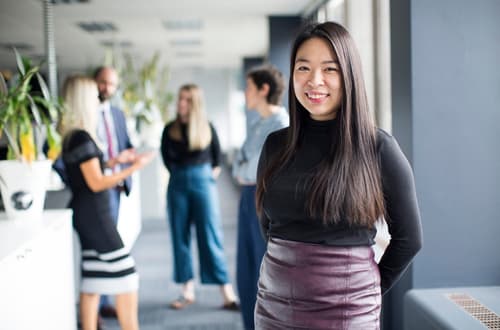 Woman smiling at camera with four people talking behind her