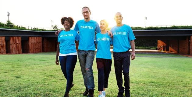 A group of four people are walking towards the camera with their arms around each other. They are all wearing blue t-shirts witch 'volunteer' written on them