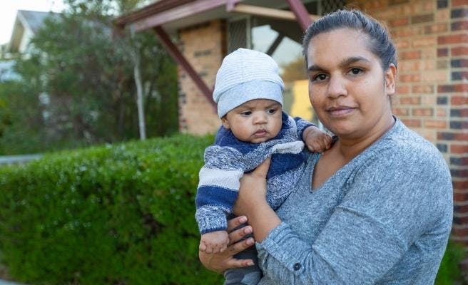 An Aboriginal woman holding her baby in the front yard