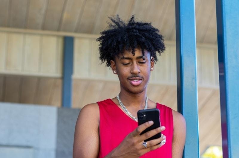 A young man leans against a post looking at his phone