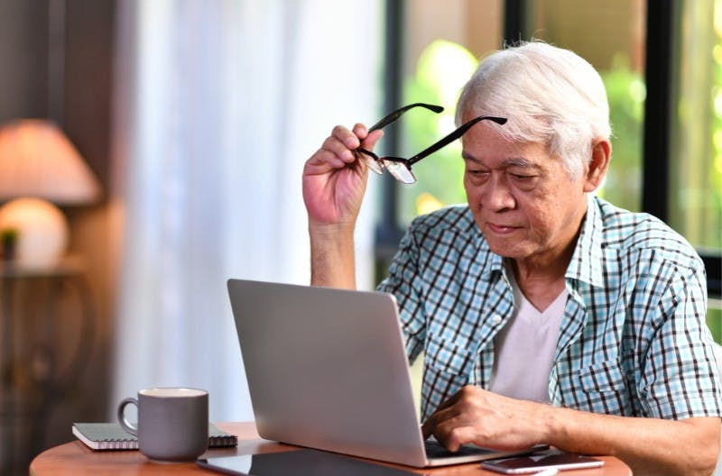 Older person takes their glasses off to look at their desktop screen.